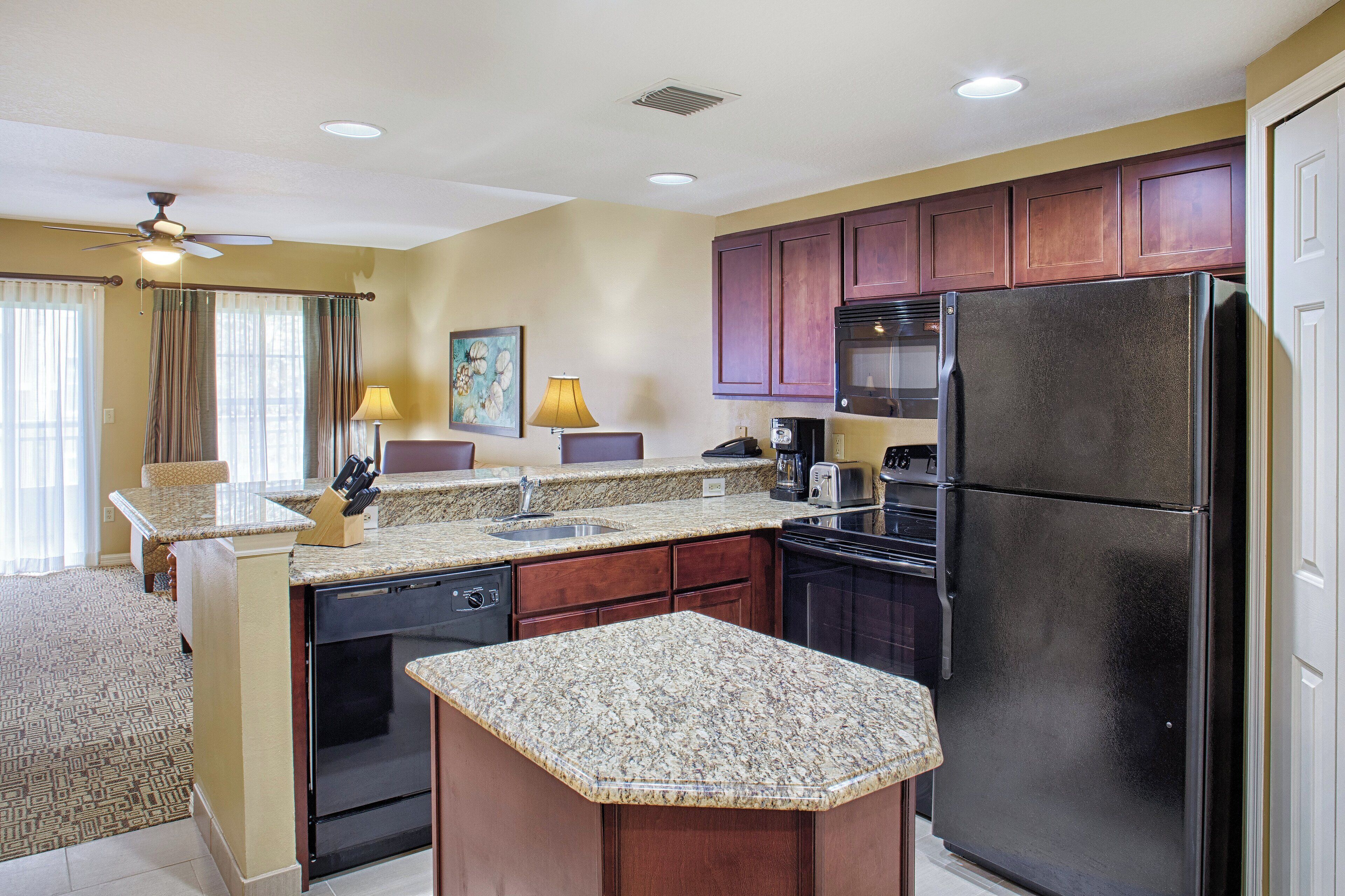 A compact kitchen with granite countertops, a refrigerator, and wooden cabinets.