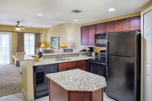 A compact kitchen with granite countertops, a refrigerator, and wooden cabinets.