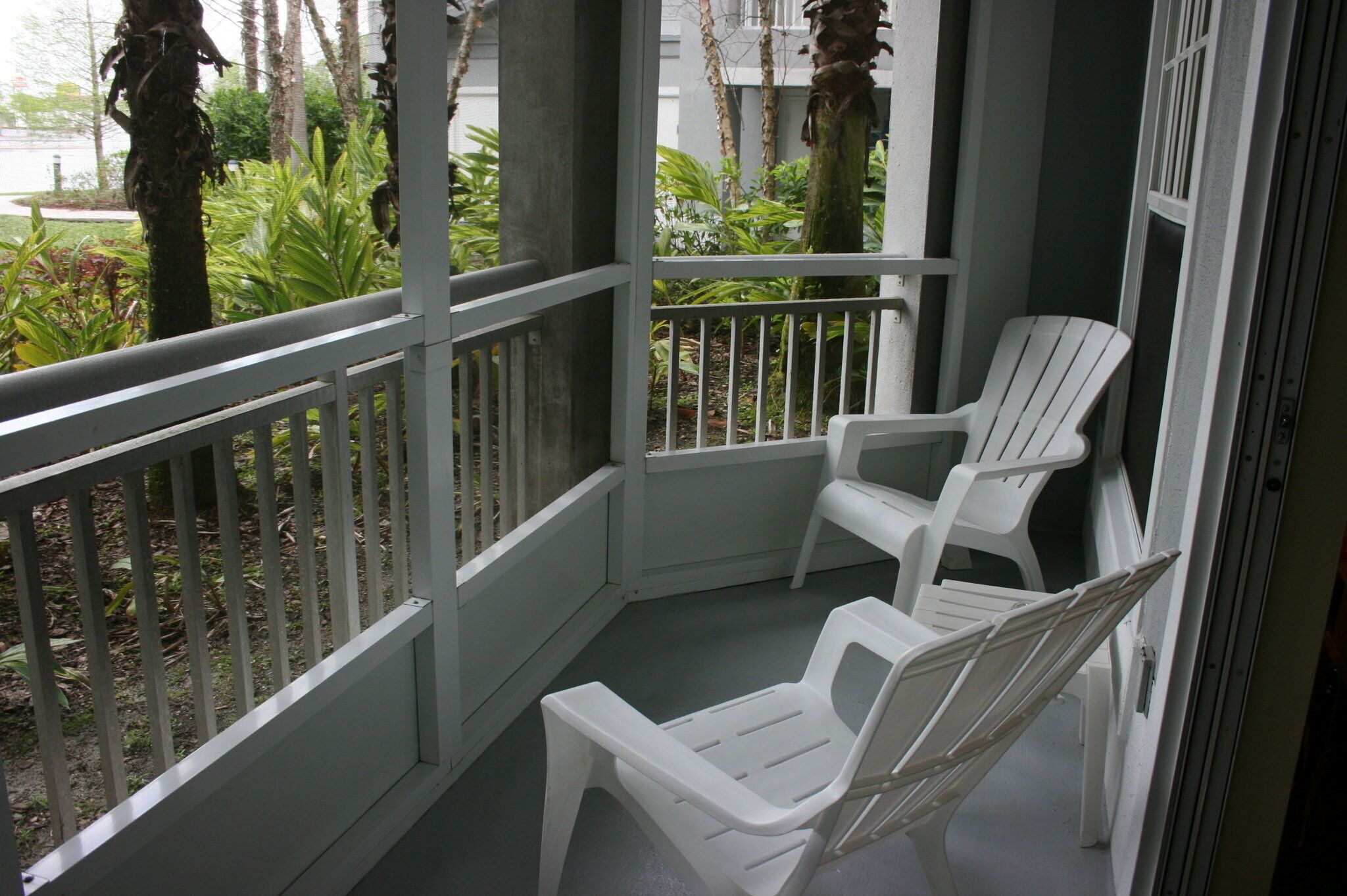 A balcony with white plastic chairs and a railing.