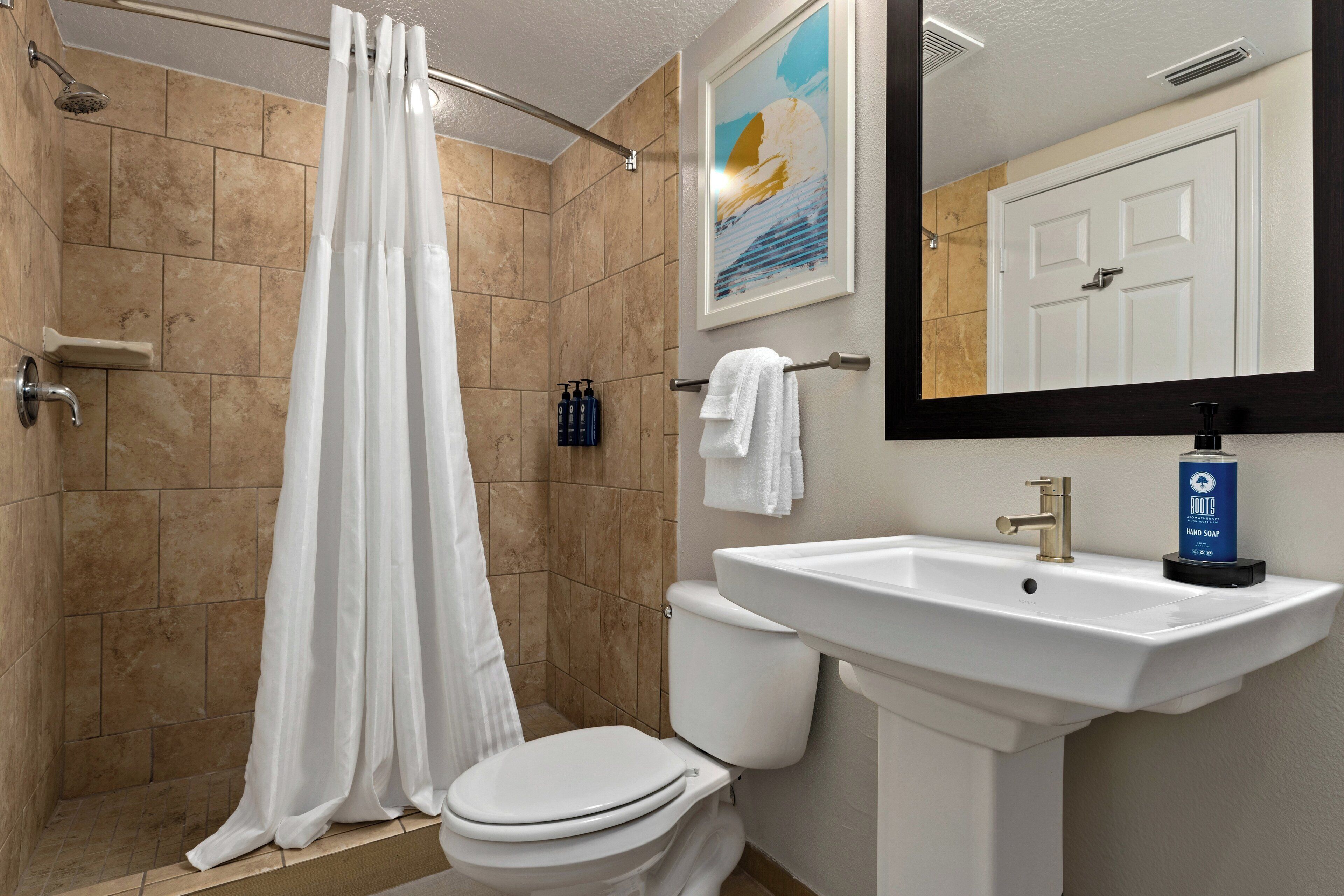A bathroom with a shower, toilet, sink, and a mirror.