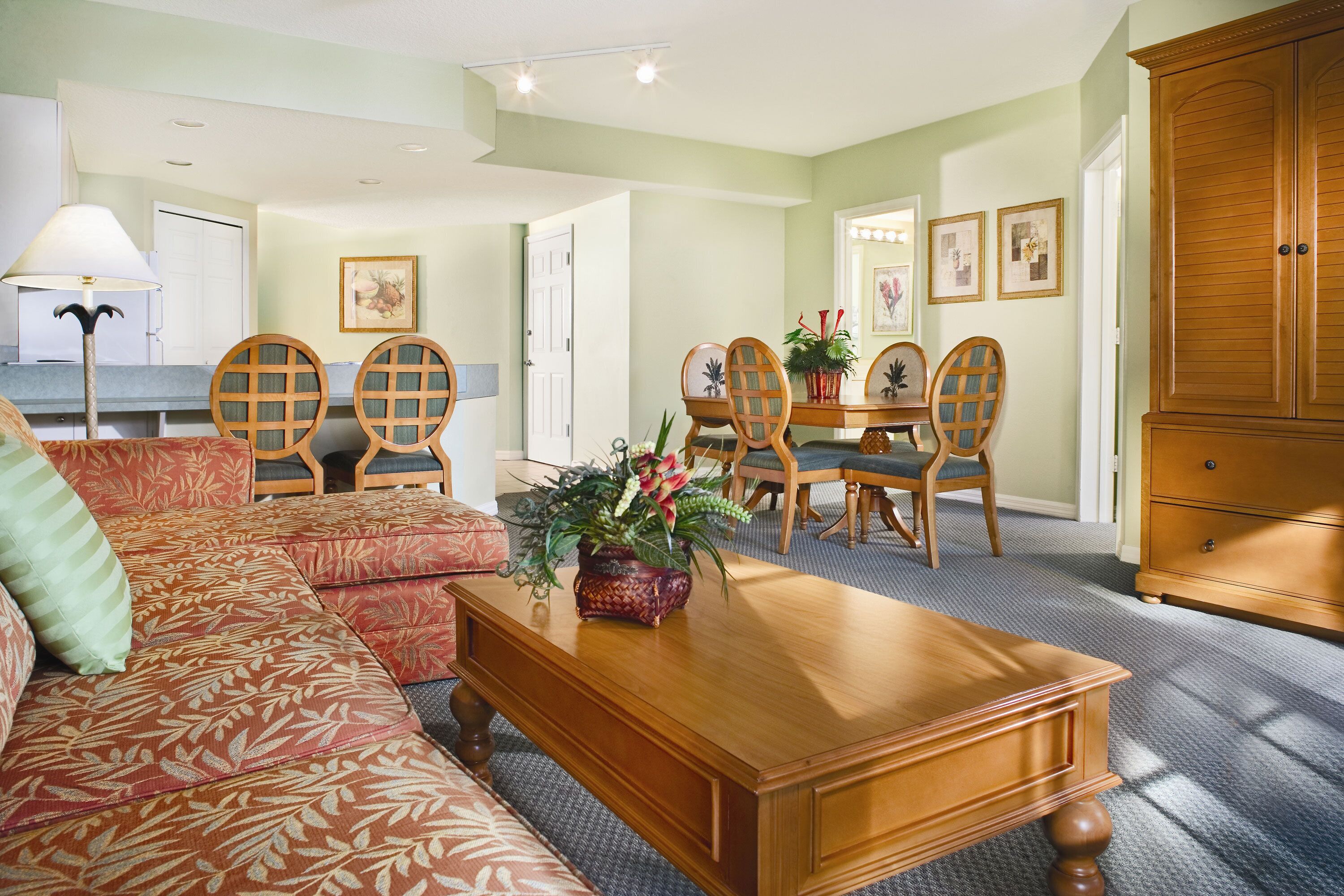 A living room with a sofa, a wooden coffee table, a dining table with chairs, and a large wooden cabinet.