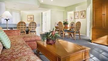 A living room with a sofa, a wooden coffee table, a dining table with chairs, and a large wooden cabinet.