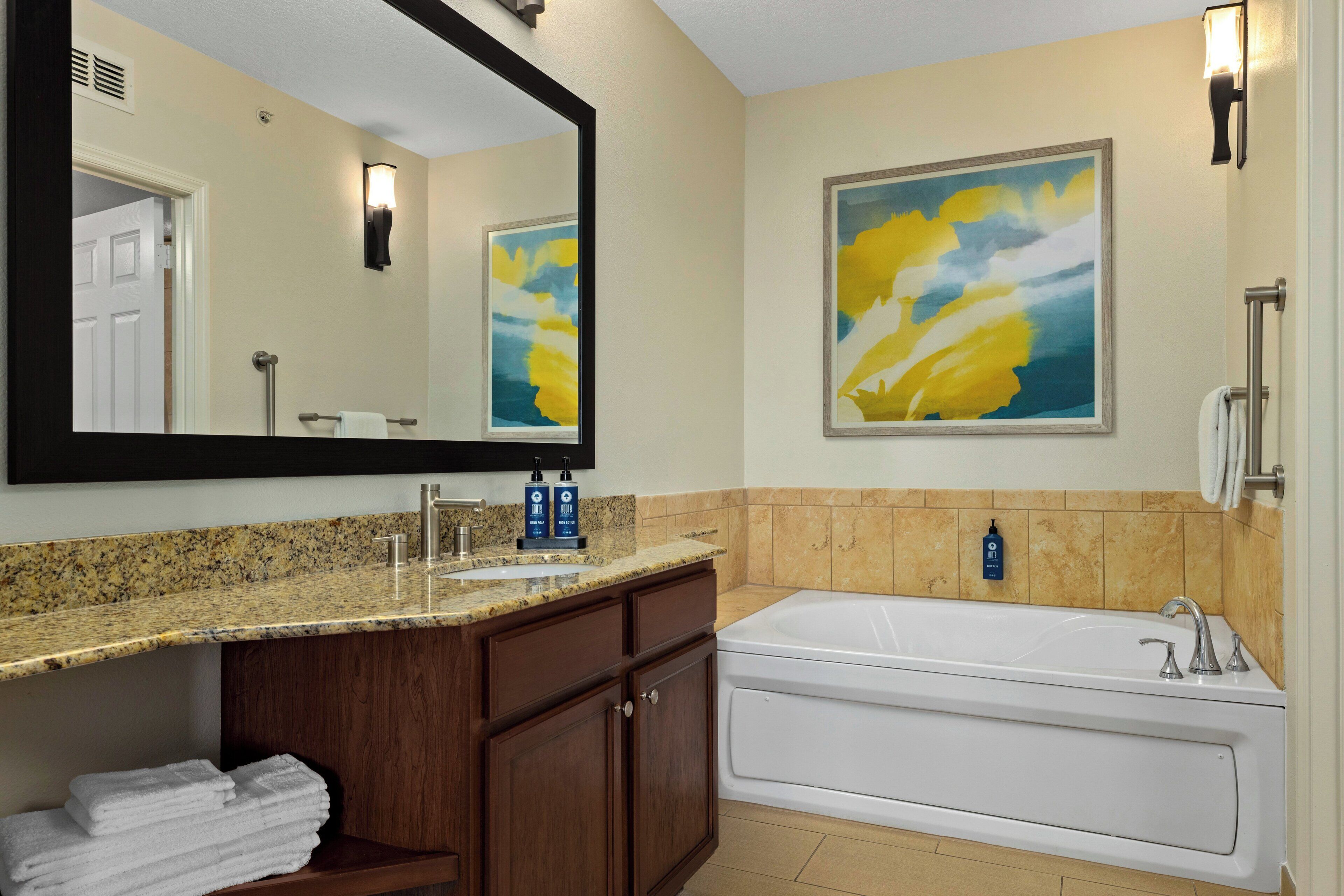 A bathroom with a granite countertop sink, a large mirror, a bathtub, and a towel rack.