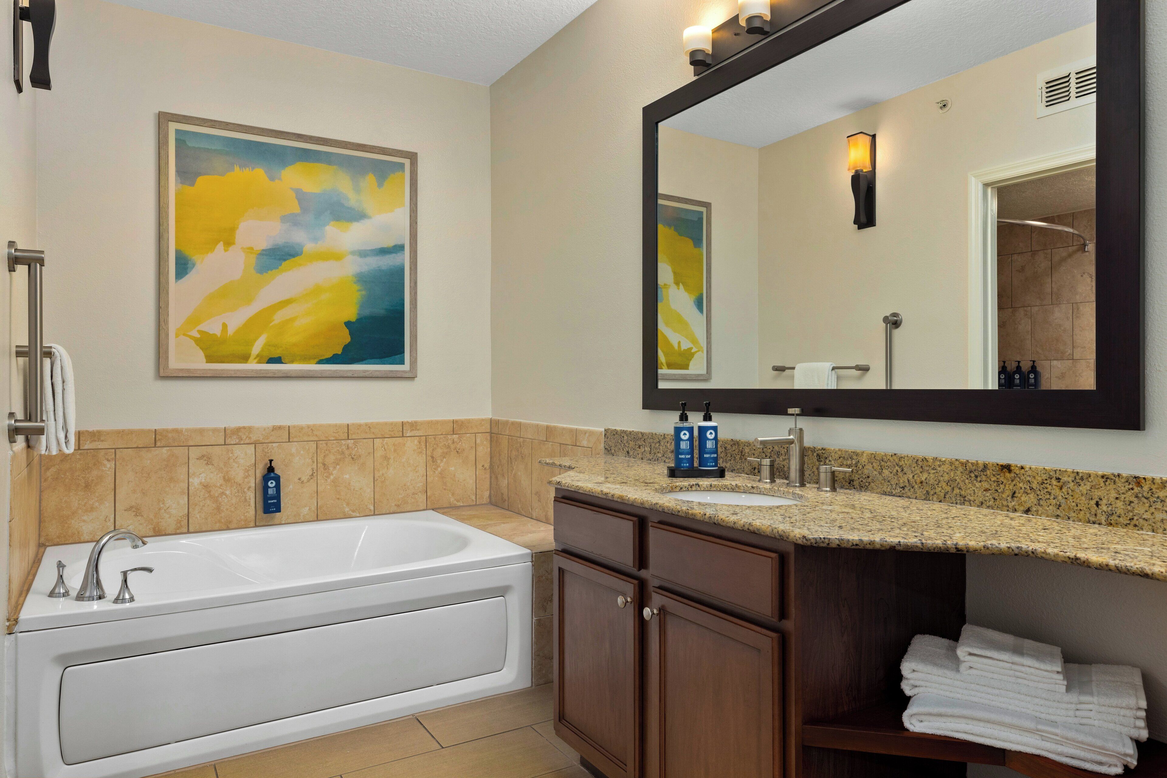 A modern bathroom with a bathtub, a sink, a large mirror, and a towel rack.