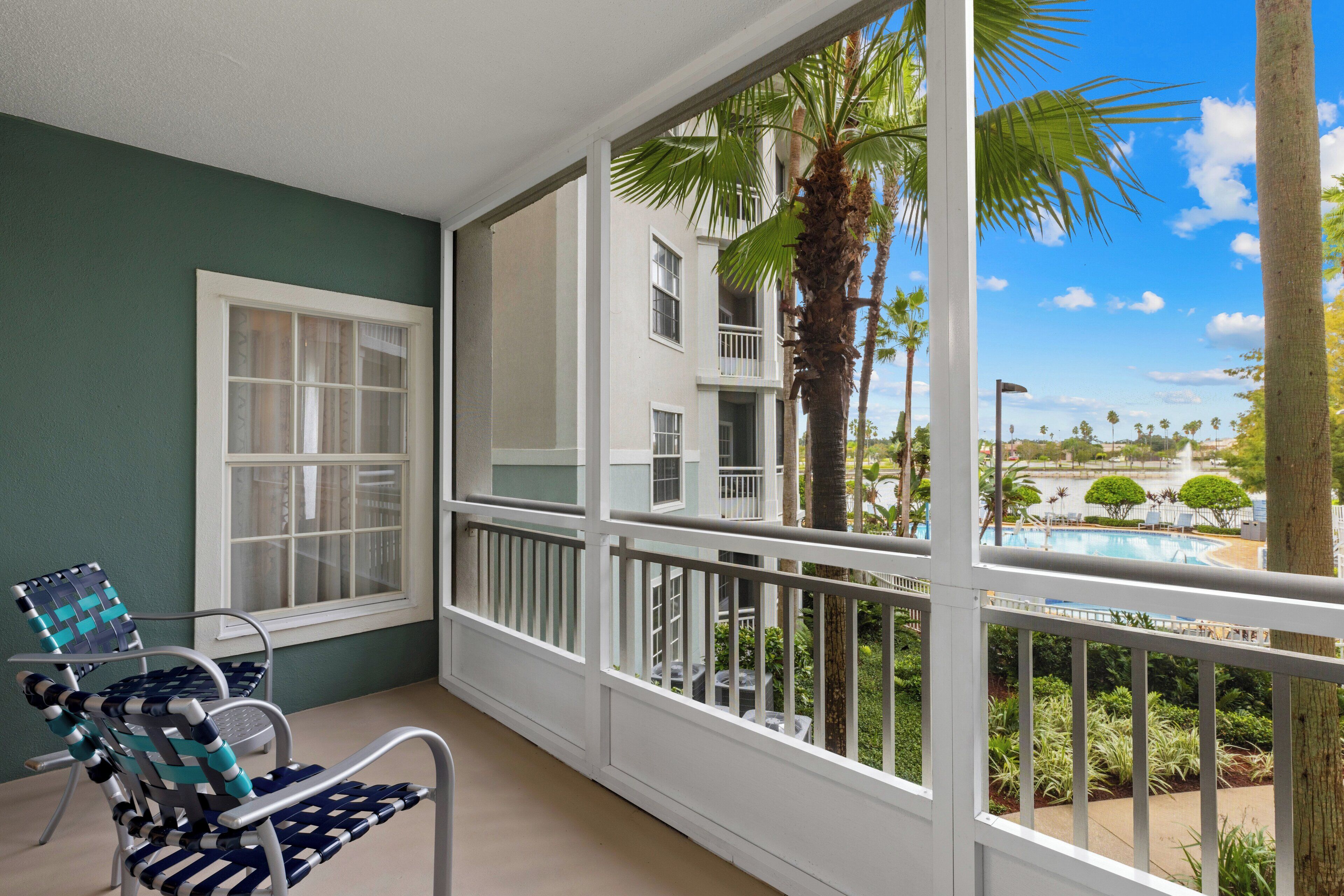 Ein Balkon mit Blick auf einen Pool und Palmen, ein Fenster sowie zwei Stühle.