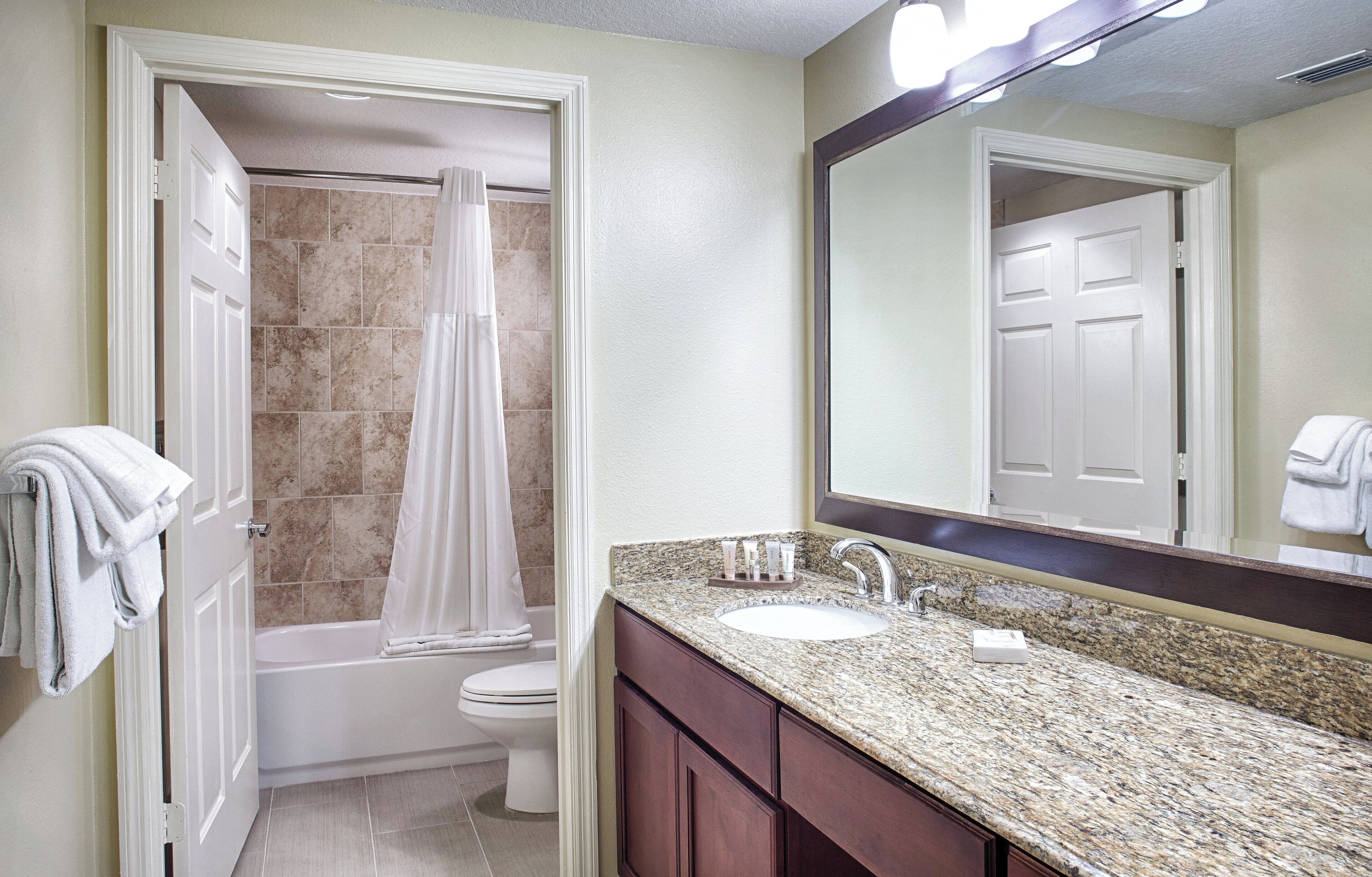 A bathroom with a shower, toilet, sink, and mirror.