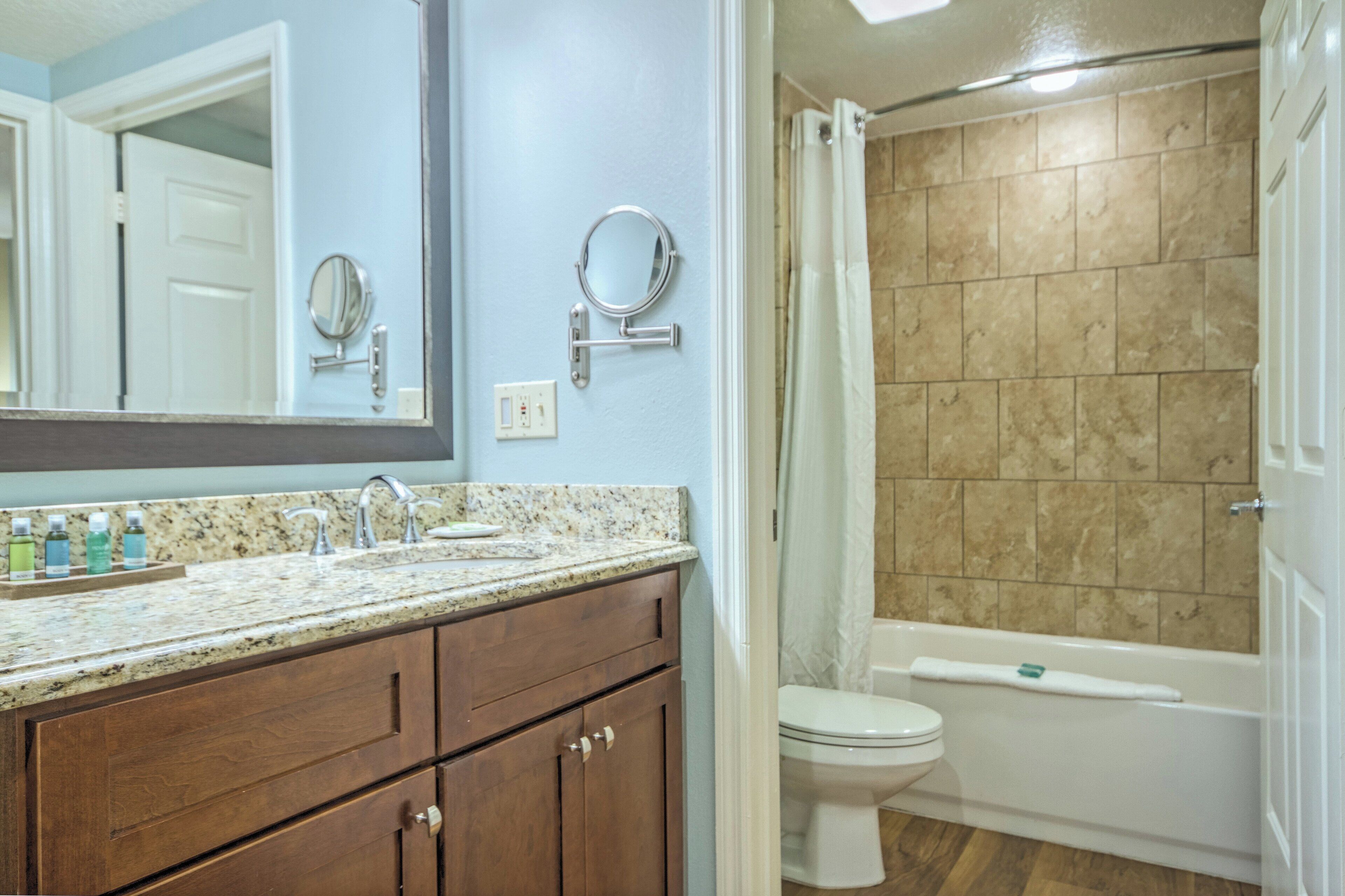 A bathroom with a granite countertop, wooden cabinets, a white toilet, and a bathtub with a shower curtain.