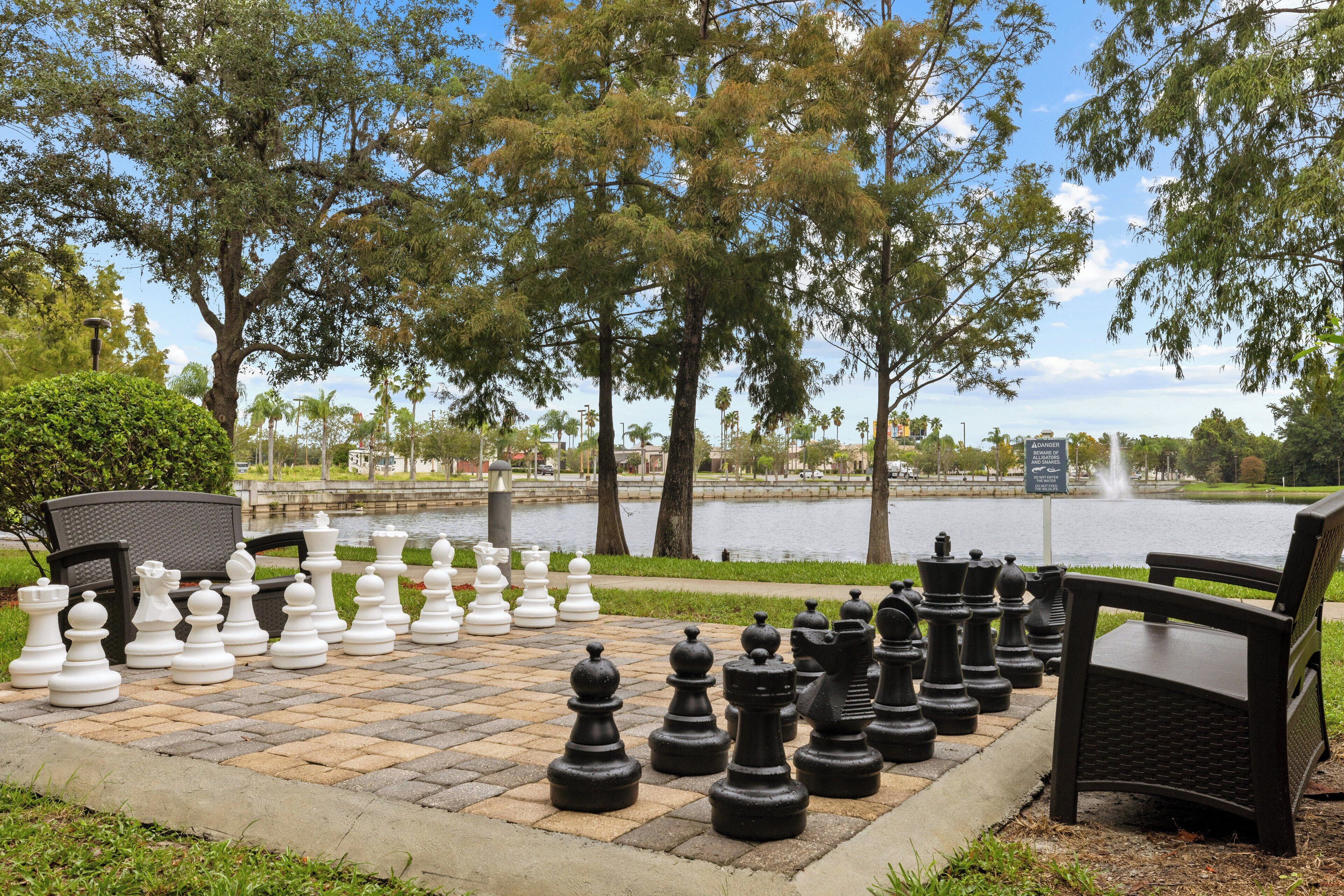 Un jeu d’échecs installé à l’extérieur, avec un banc et des arbres en arrière-plan.