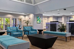 A modern lobby with seating areas, a reception desk, and a large window offering a view of the outdoors.