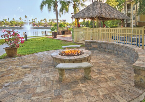 A stone fire pit with benches, a thatched-roof structure, and a view of a body of water.