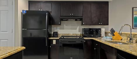 A modern kitchen with dark cabinetry, a built-in oven, a microwave, and a granite countertop.