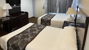 A hotel room with two beds, a desk, a dresser, a ceiling fan, a TV, and a window with curtains. - Hollywood Guest Inn (Los Angeles)