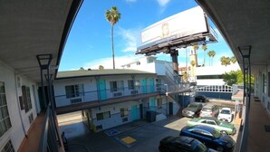 A parking area with several cars, a building with a blue and white facade, and a billboard above. - Hollywood Guest Inn (Los Angeles)