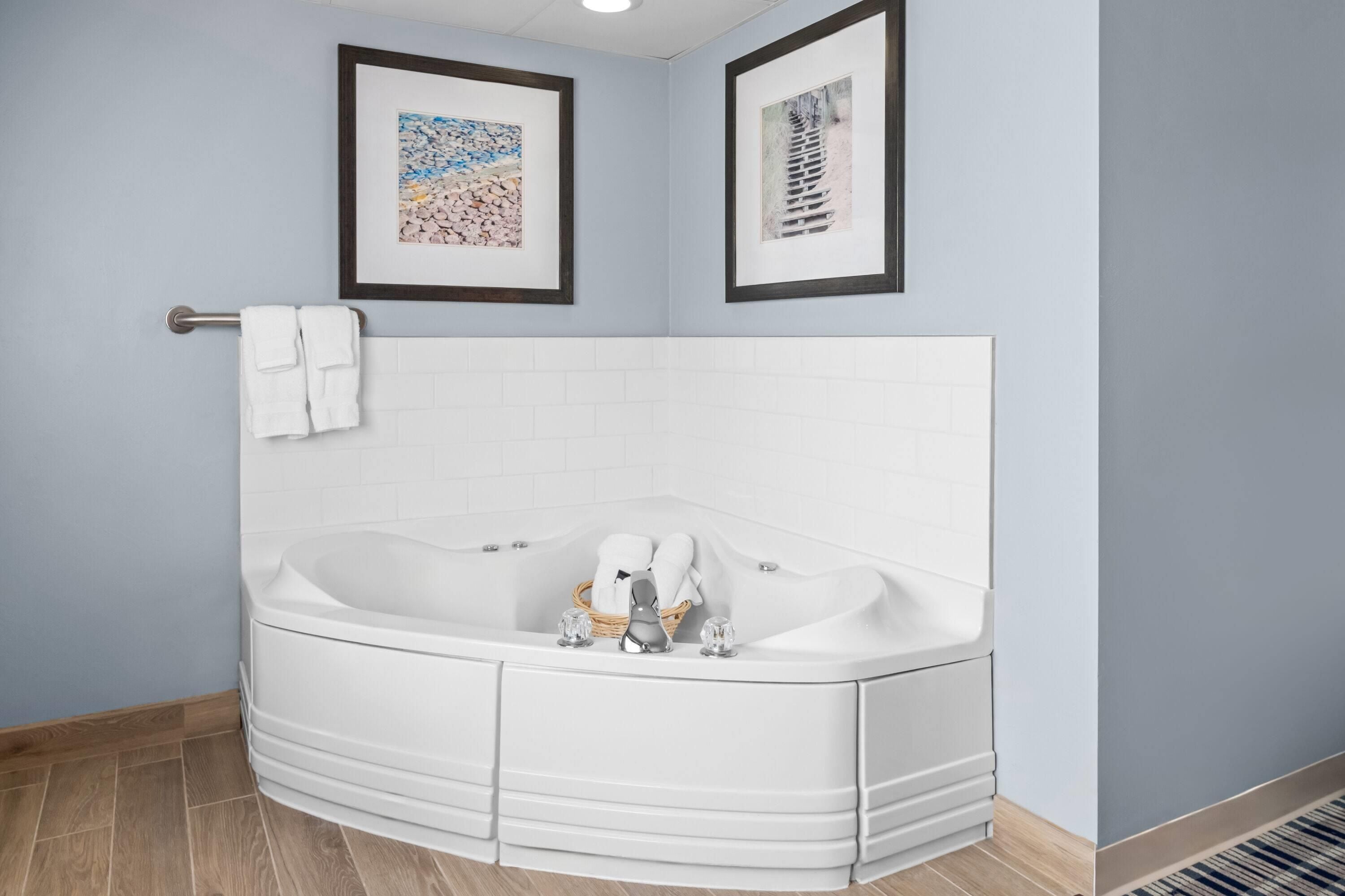 Un baño moderno con una bañera independiente, azulejos blancos y dos cuadros enmarcados en la pared.