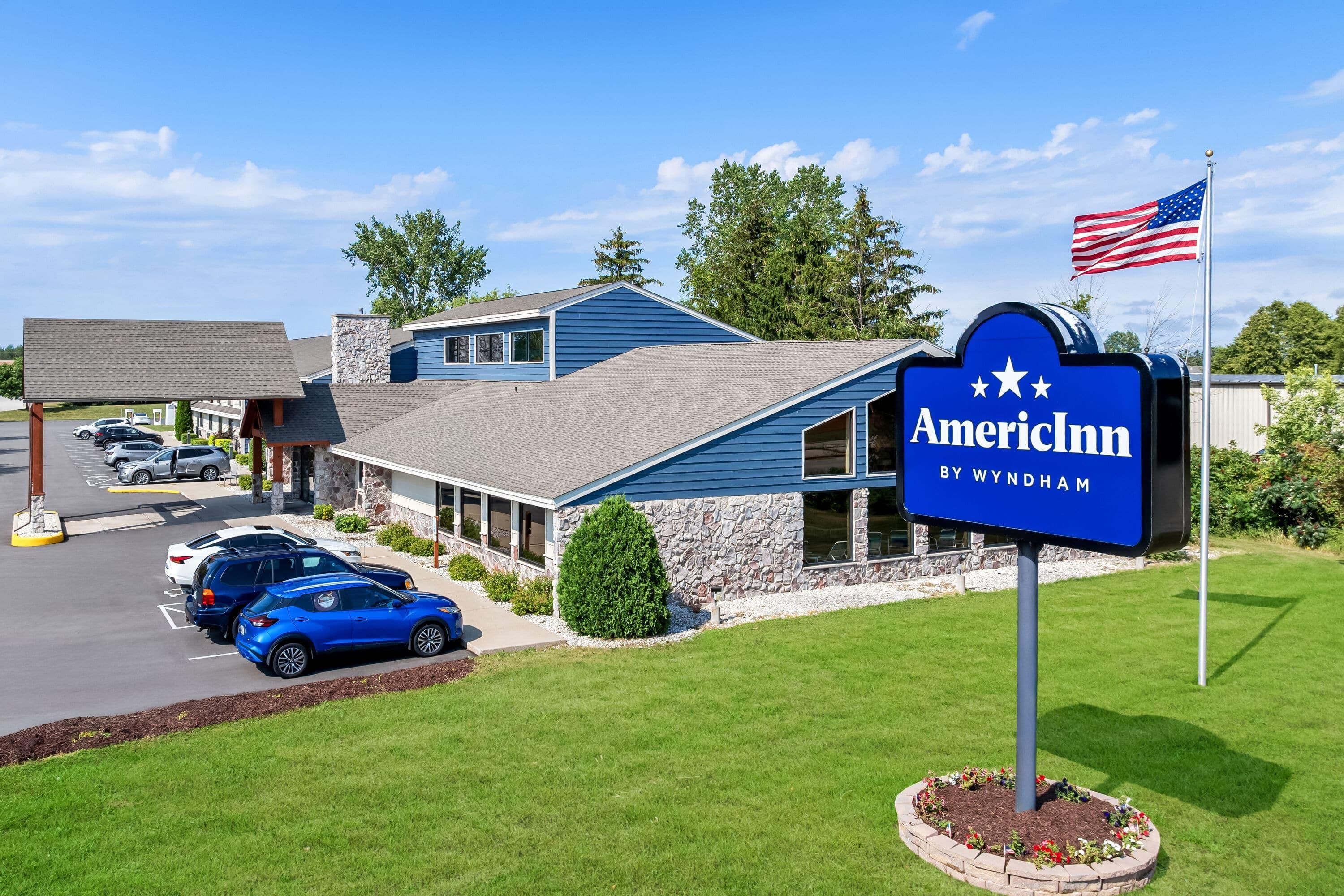 Un hôtel de la chaîne American Inn by Wyndham, avec une façade bleue, des éléments décoratifs en pierre et un parking où sont stationnées plusieurs voitures.