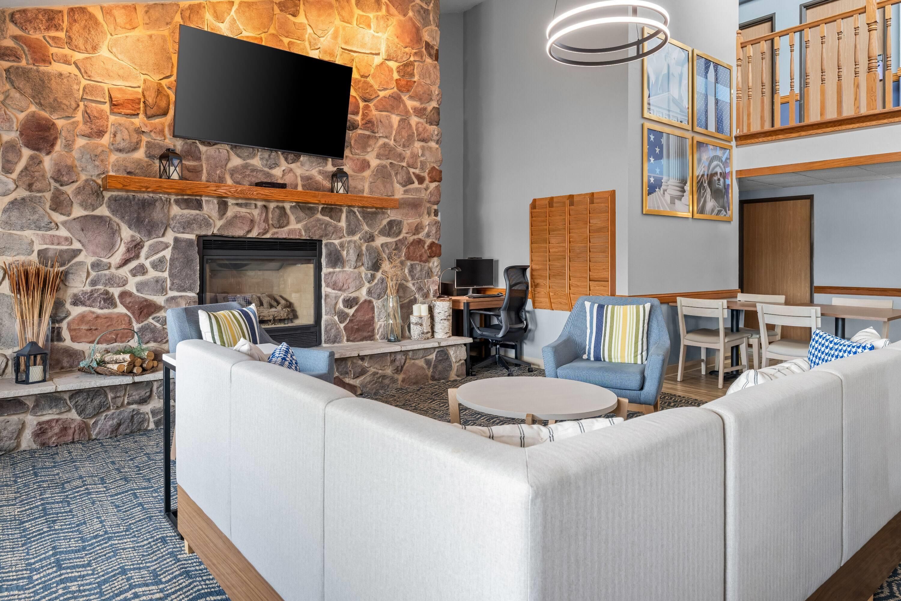Ein modernes Wohnzimmer mit Steinwand, Kamin, Flachbildfernseher und einer Sitzecke mit Sofas und Sesseln.