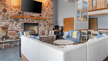 A modern living room with a stone wall, a fireplace, a flat-screen TV, and a seating area with sofas and chairs.