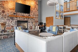A modern living room with a stone wall, a fireplace, a flat-screen TV, and a seating area with sofas and chairs.