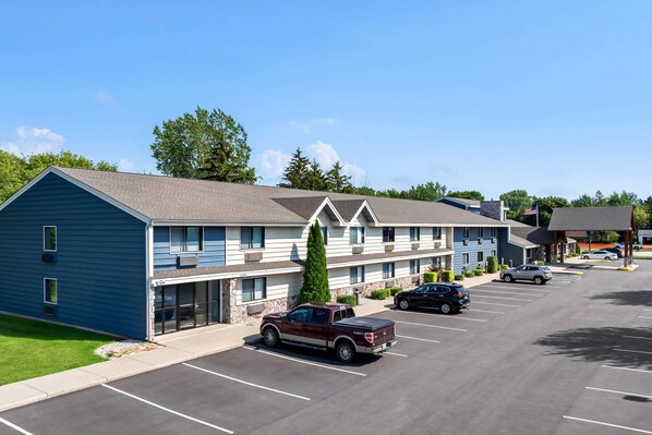 A multi-story hotel with a parking lot, a red pickup truck, and a black SUV parked. - AmericInn by Wyndham Sturgeon Bay (Sturgeon Bay)