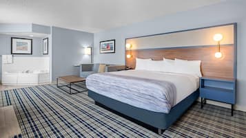 Ein modernes Hotelzimmer mit einem großen Bett, einem Nachttisch, einem Schreibtisch, einem Sessel und einem Badezimmer mit einer Badewanne sowie zwei Wandleuchten.