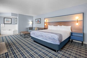 Una habitación de hotel moderna con una cama grande, una mesita de noche, un escritorio, una silla, un baño con bañera y dos lámparas de pared.