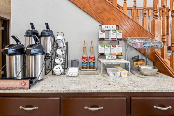 A coffee station with two coffee makers, a Torani syrup dispenser, and a Torani Classic Caramel Hazelnut bottle. - AmericInn by Wyndham Sturgeon Bay (Sturgeon Bay)
