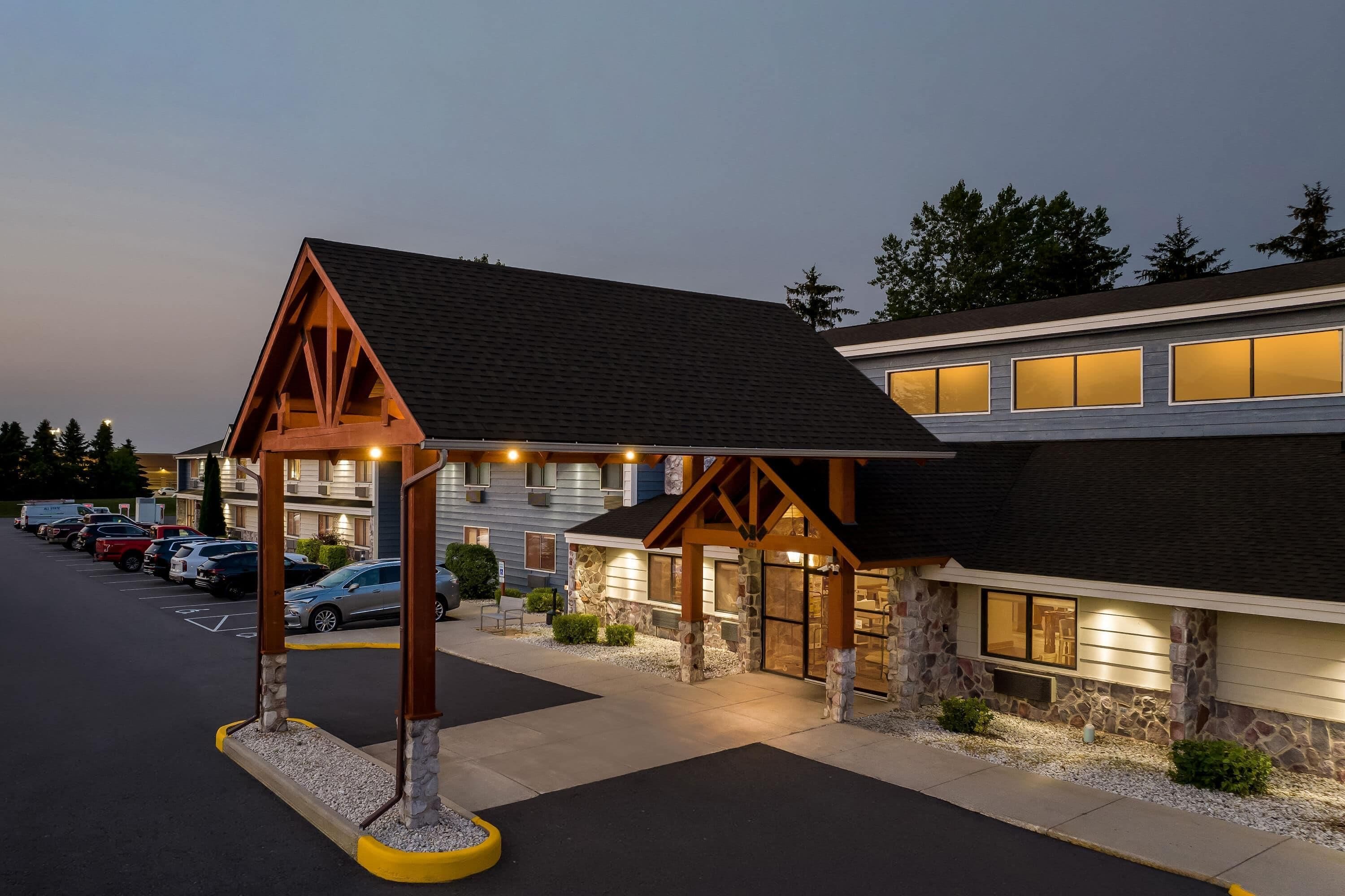 A hotel with a covered entrance, stone facade, and a parking lot with several cars.