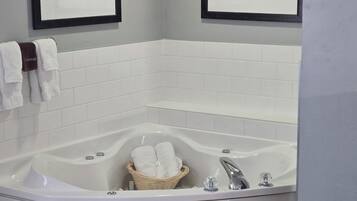 Un baño en esquina con bañera independiente, paredes de azulejos blancos y dos cuadros enmarcados.