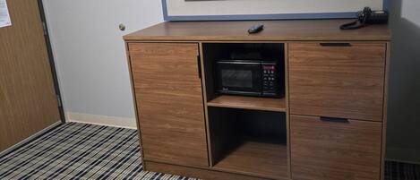 A hotel room with a large flat-screen TV mounted on the wall, a wooden cabinet with a microwave, and a striped carpet.