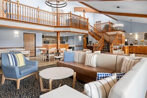 Een ruime hotellobby met een hoge plafond, een centraal zitgedeelte met banken en stoelen, een trap die twee verdiepingen verbindt, en een receptiebalie.