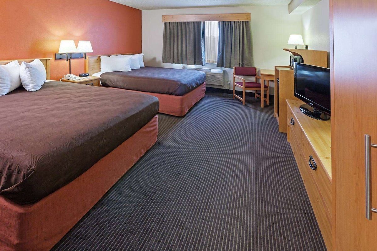 Een hotelkamer met twee bedden, een bureau, een stoel, een televisie en een raam met gordijnen.