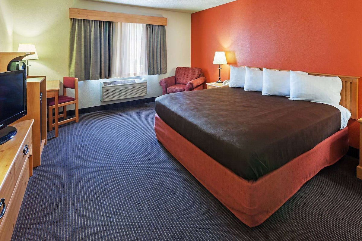 Een hotelkamer met een groot bed, een bureau met een televisie, een stoel en een raam met gordijnen.