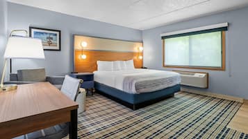A hotel room with a bed, bedside table, lamp, and a large window.