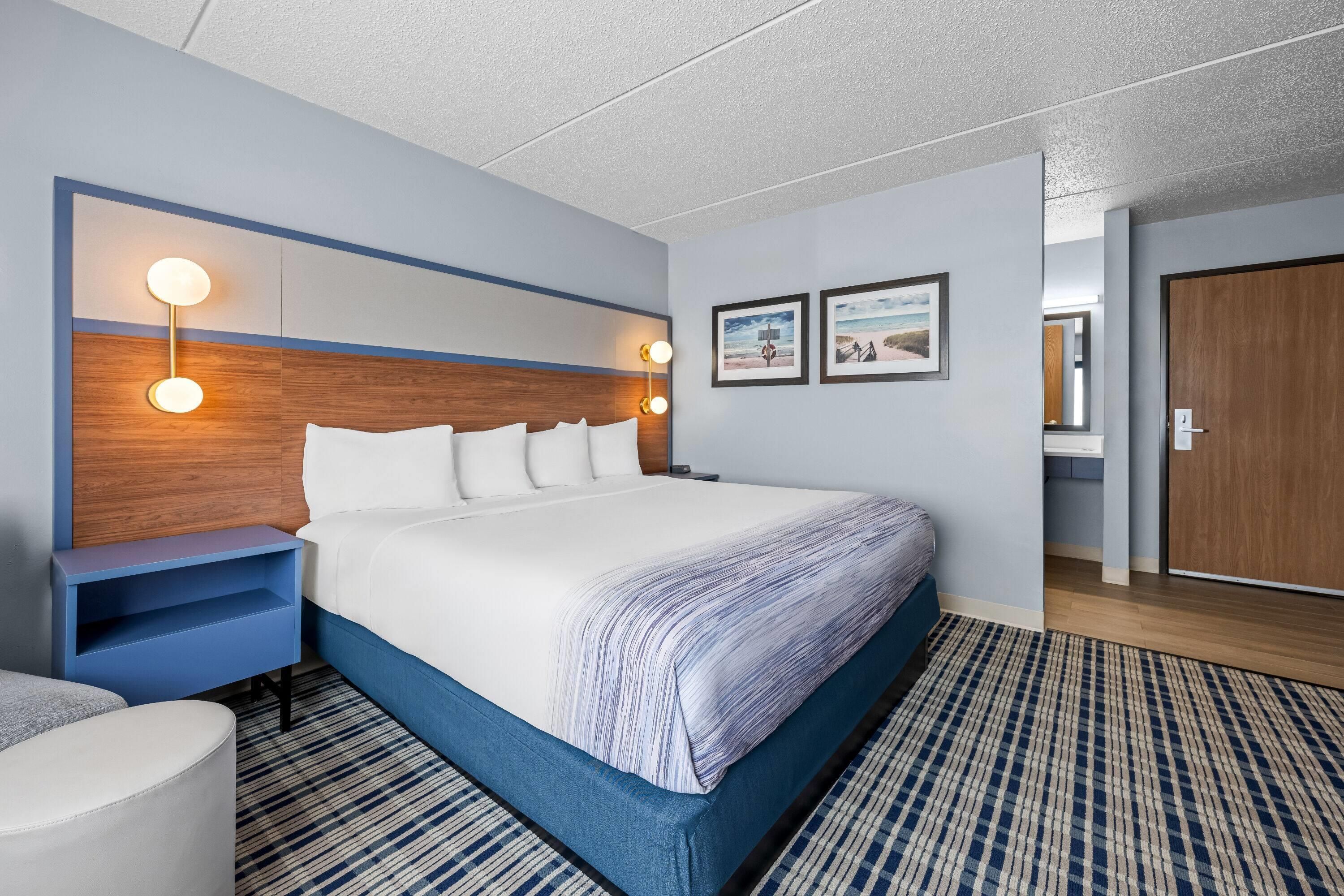 A hotel room with a large bed, bedside tables, wall-mounted lights, and two framed pictures.