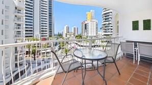 A balcony with a round table and chairs, overlooking a cityscape with modern buildings. - Phoenician Resort (Broadbeach)