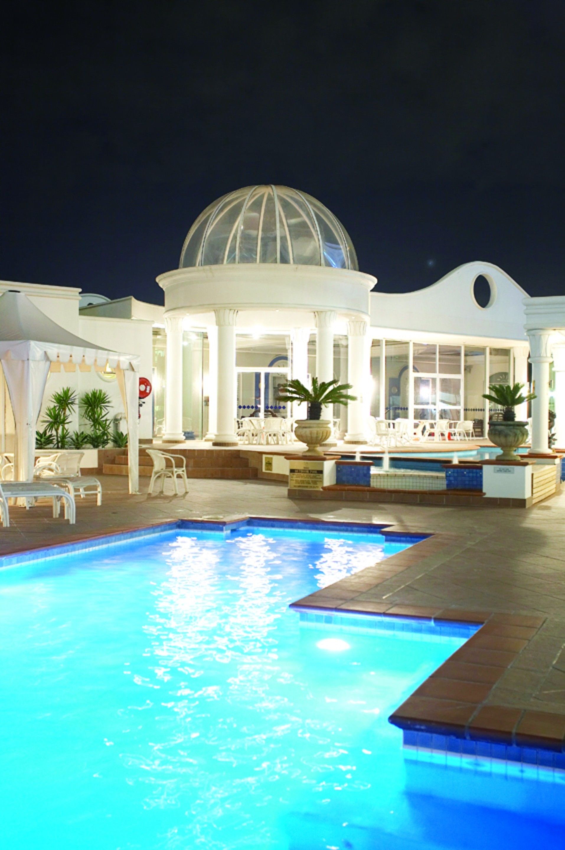 A swimming pool with a dome structure in the background, surrounded by lounge chairs and potted plants.