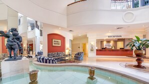 A spacious lobby with a reception desk, seating area, and a central pool. - Phoenician Resort (Broadbeach)
