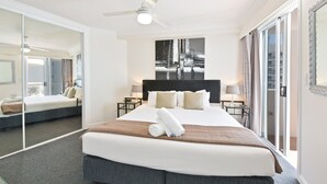 A hotel room with a large bed, a ceiling fan, a cityscape painting, and a sliding glass door to the outside. - Phoenician Resort (Broadbeach)