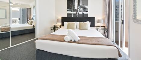 A hotel room with a large bed, a ceiling fan, a cityscape painting, and a sliding glass door to the outside.