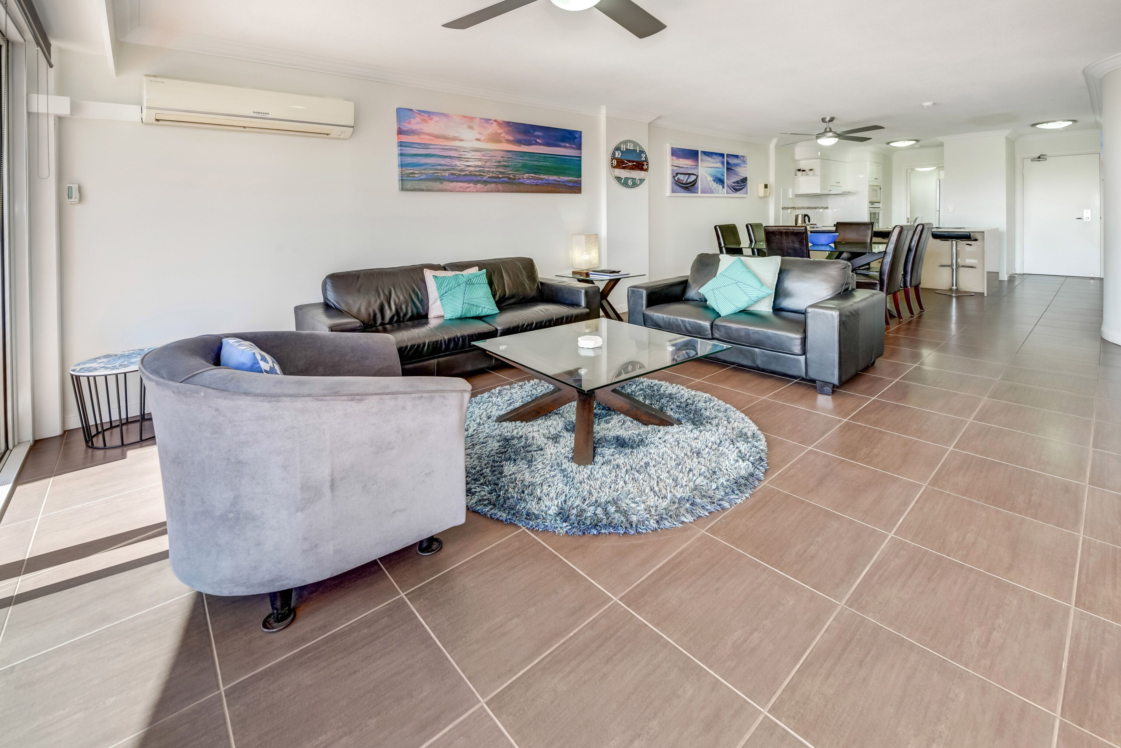 A modern living room with a glass coffee table, leather sofas, and a round rug.