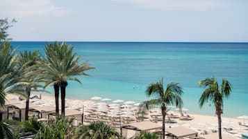 Una playa con palmeras, sombrillas y sillones de descanso.