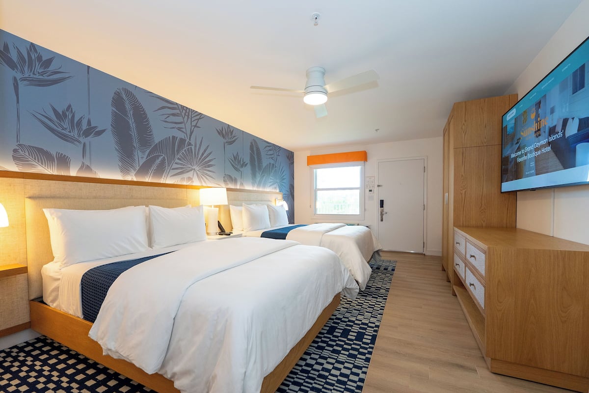 A hotel room with two beds, a ceiling fan, a TV, and a large window.
