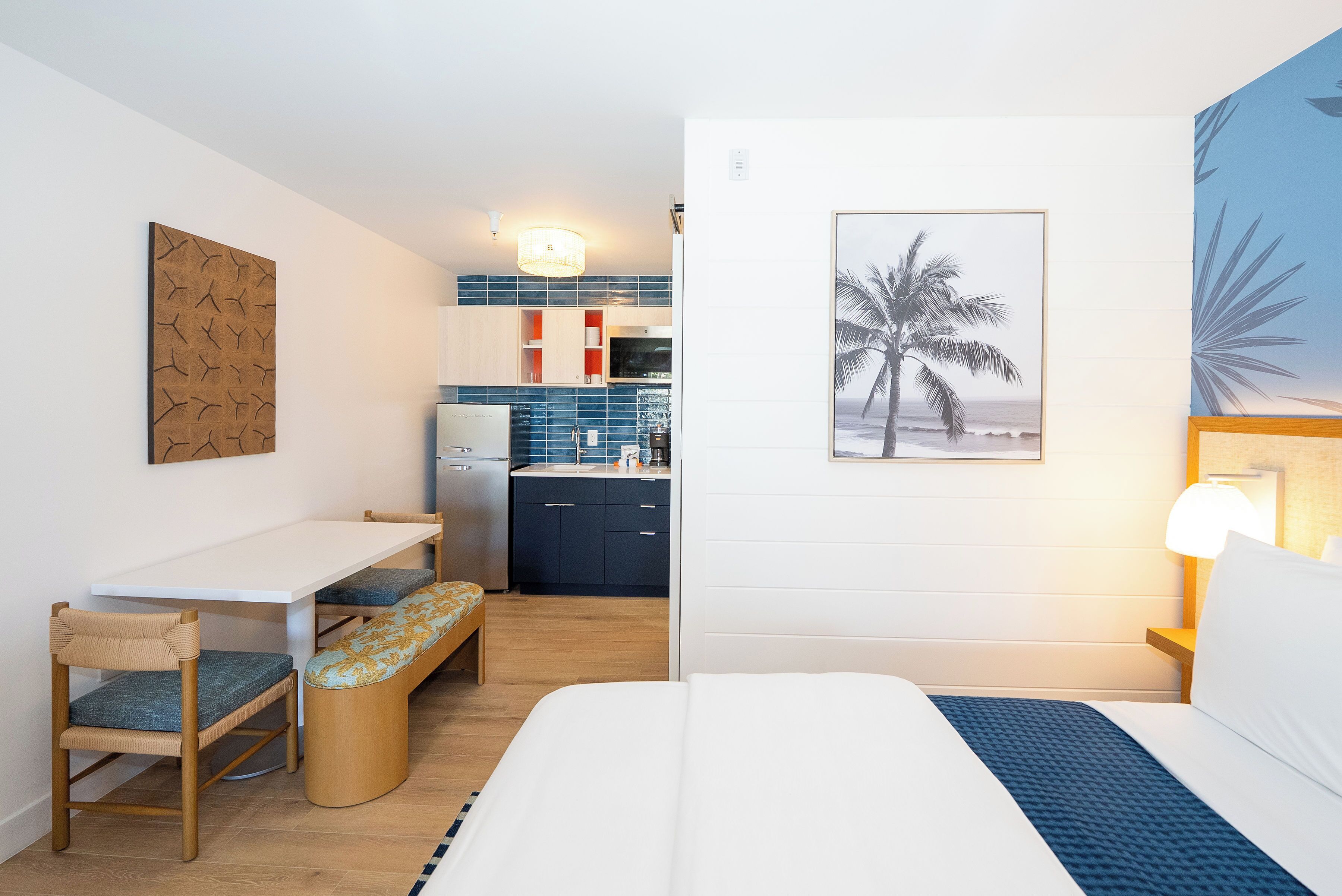Quarto de hotel compacto com cozinha compacta, área de refeições e cama com detalhes em azul.