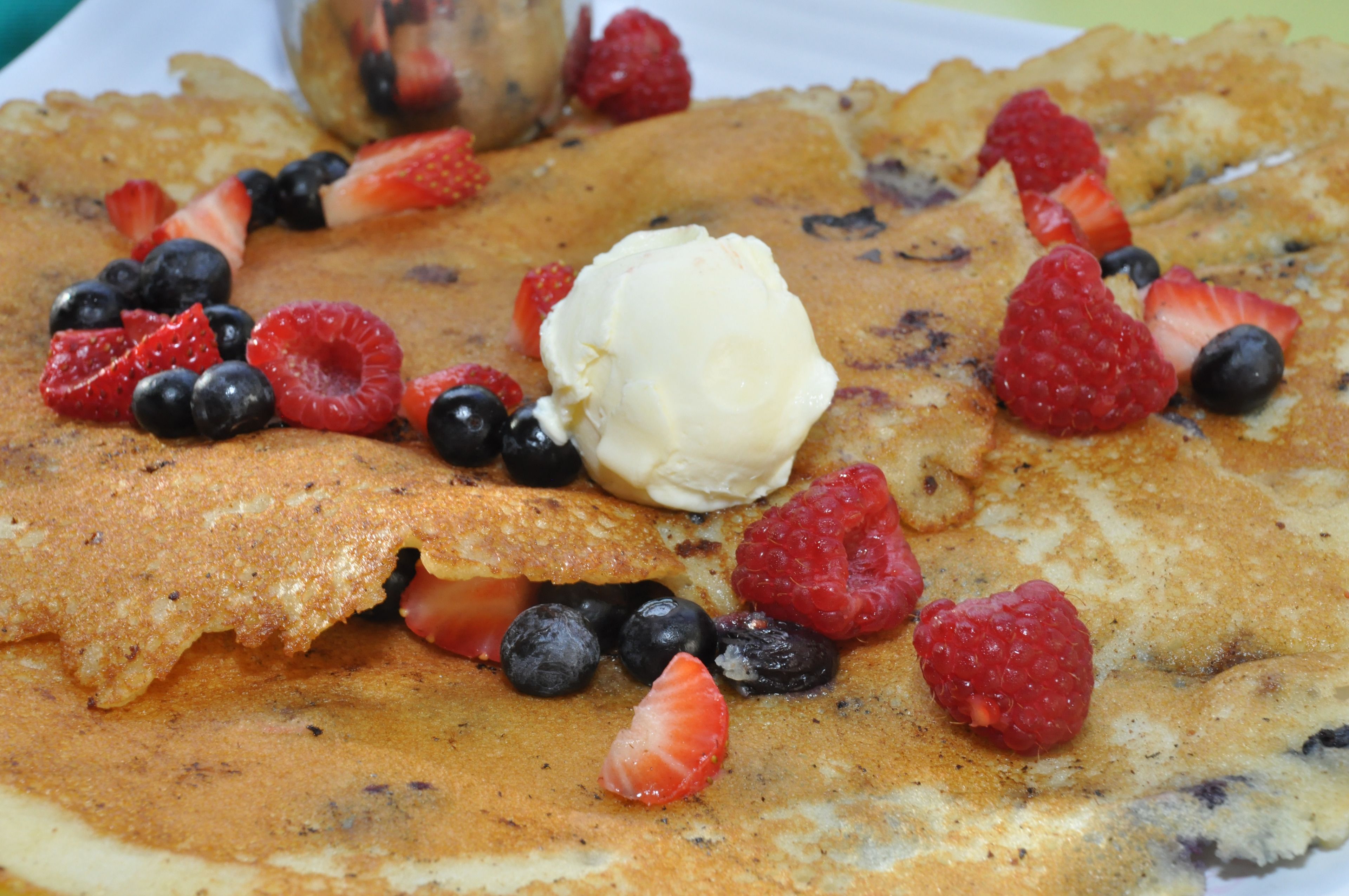 A stack of pancakes topped with strawberries, blueberries, raspberries, and a scoop of ice cream.