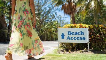 A woman in a floral dress walking past a sign indicating beach access.
