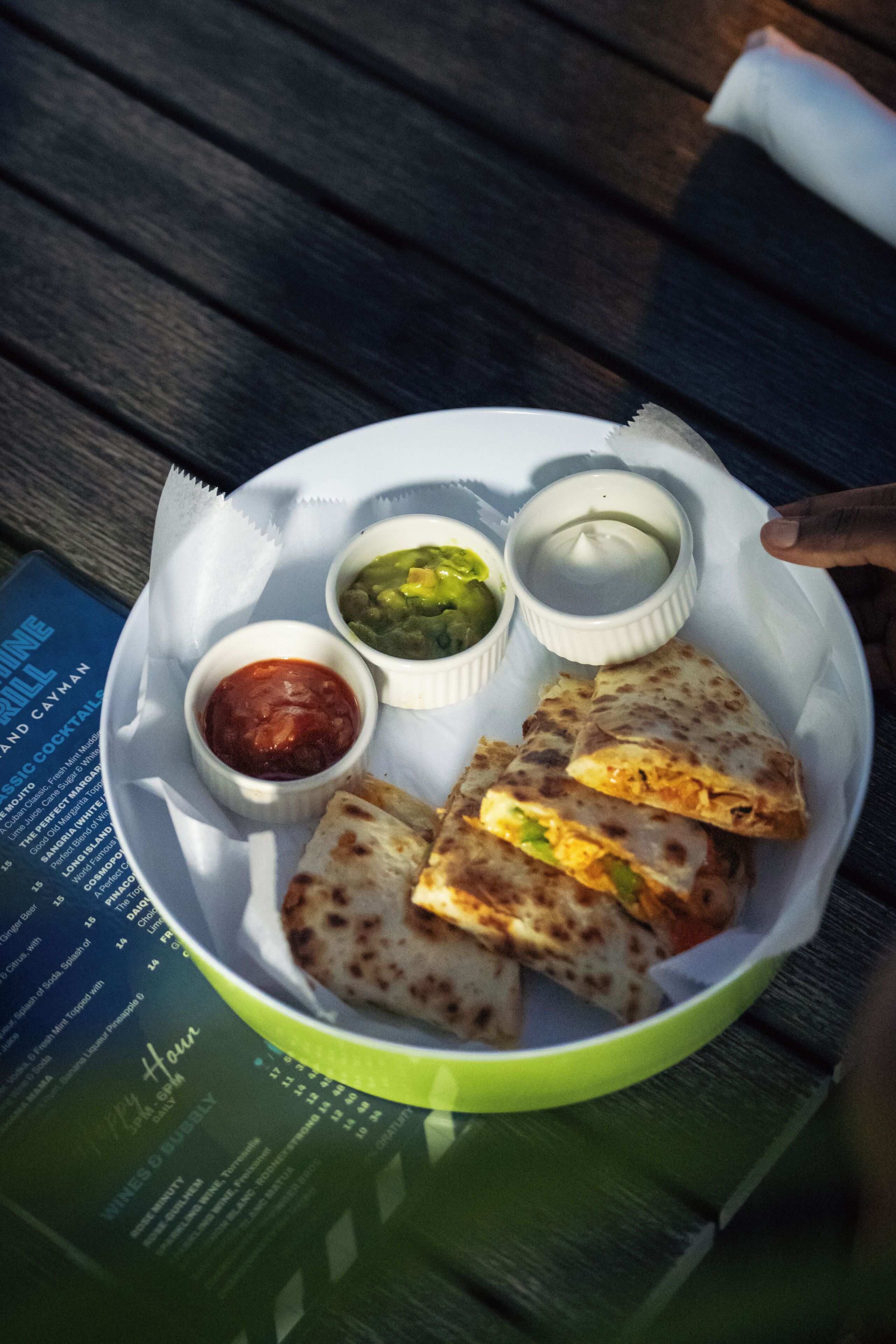 A plate with quesadillas and three dipping sauces on a table.