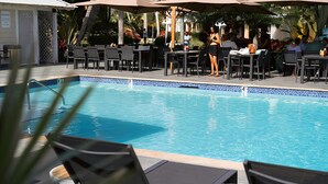A swimming pool with lounge chairs and tables, surrounded by umbrellas and a tropical setting. - The Sunshine Hotel and Suites (Seven Mile Beach)