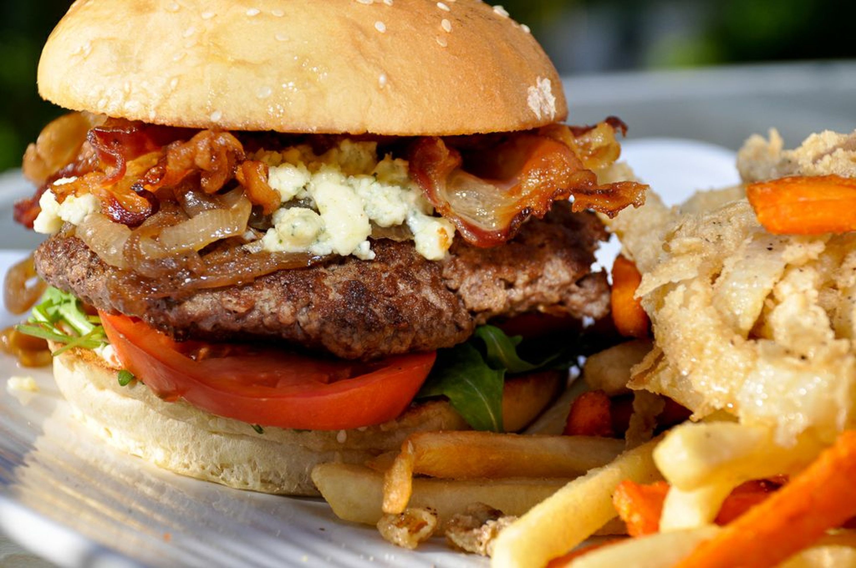 A burger with bacon, onions, and cheese on a bun, accompanied by fries and a side salad.