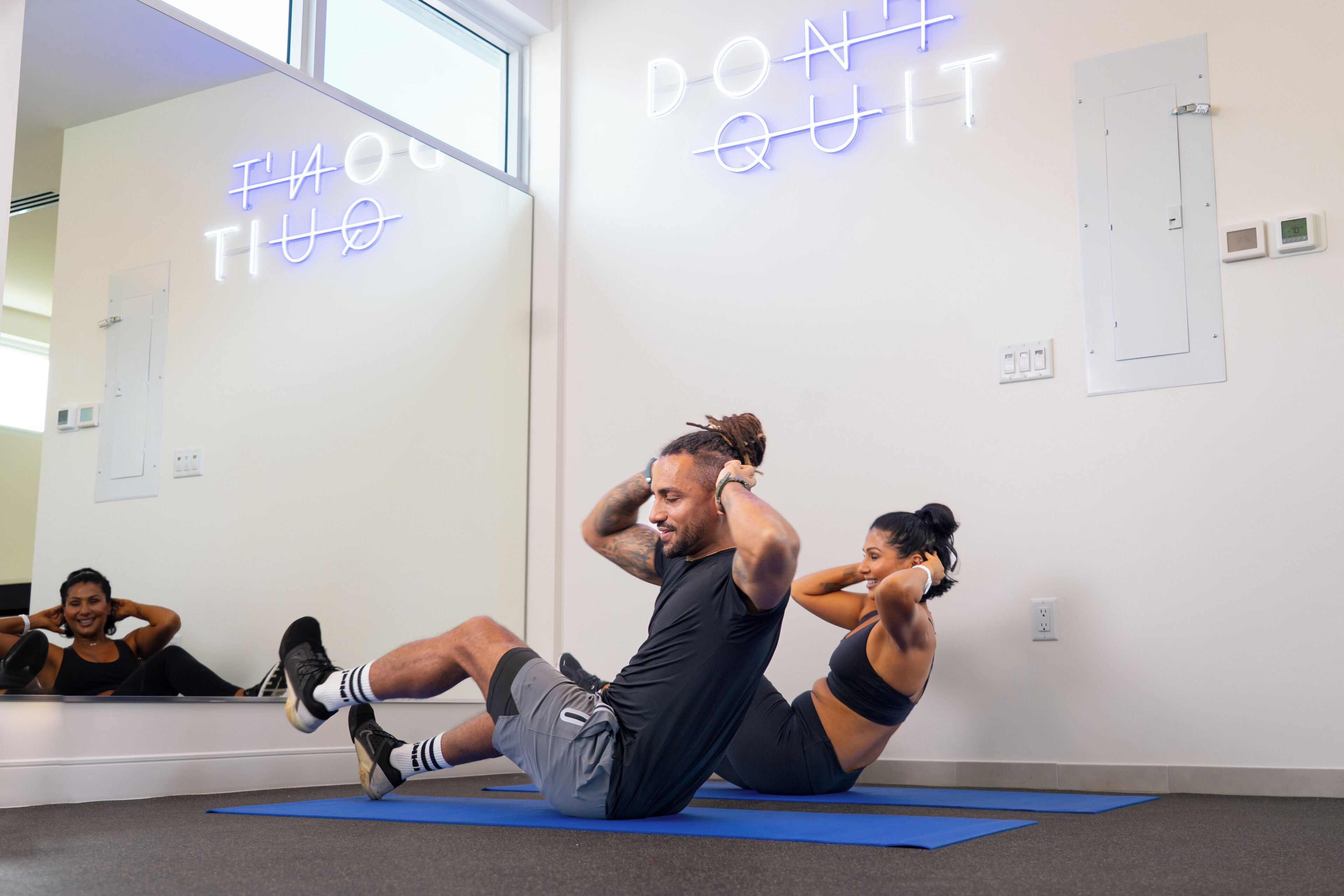 Un estudio de fitness con colchonetas de ejercicio, un letrero de neón motivacional y un espejo grande.