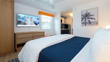 Une chambre d’hôtel avec un lit, un téléviseur fixé au mur, un ventilateur de plafond, une fenêtre et un tableau représentant un palmier.